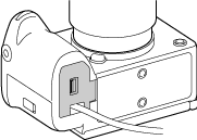 Ilustración de una tapa del compartimento de la batería (se vende por separado) acoplada con un acoplador CC (se vende por separado) conectado.