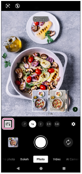 Immagine che mostra l'icona personalizzata per la funzione AI Camera Assistant sul lato inferiore sinistro del mirino in modalità [Foto].